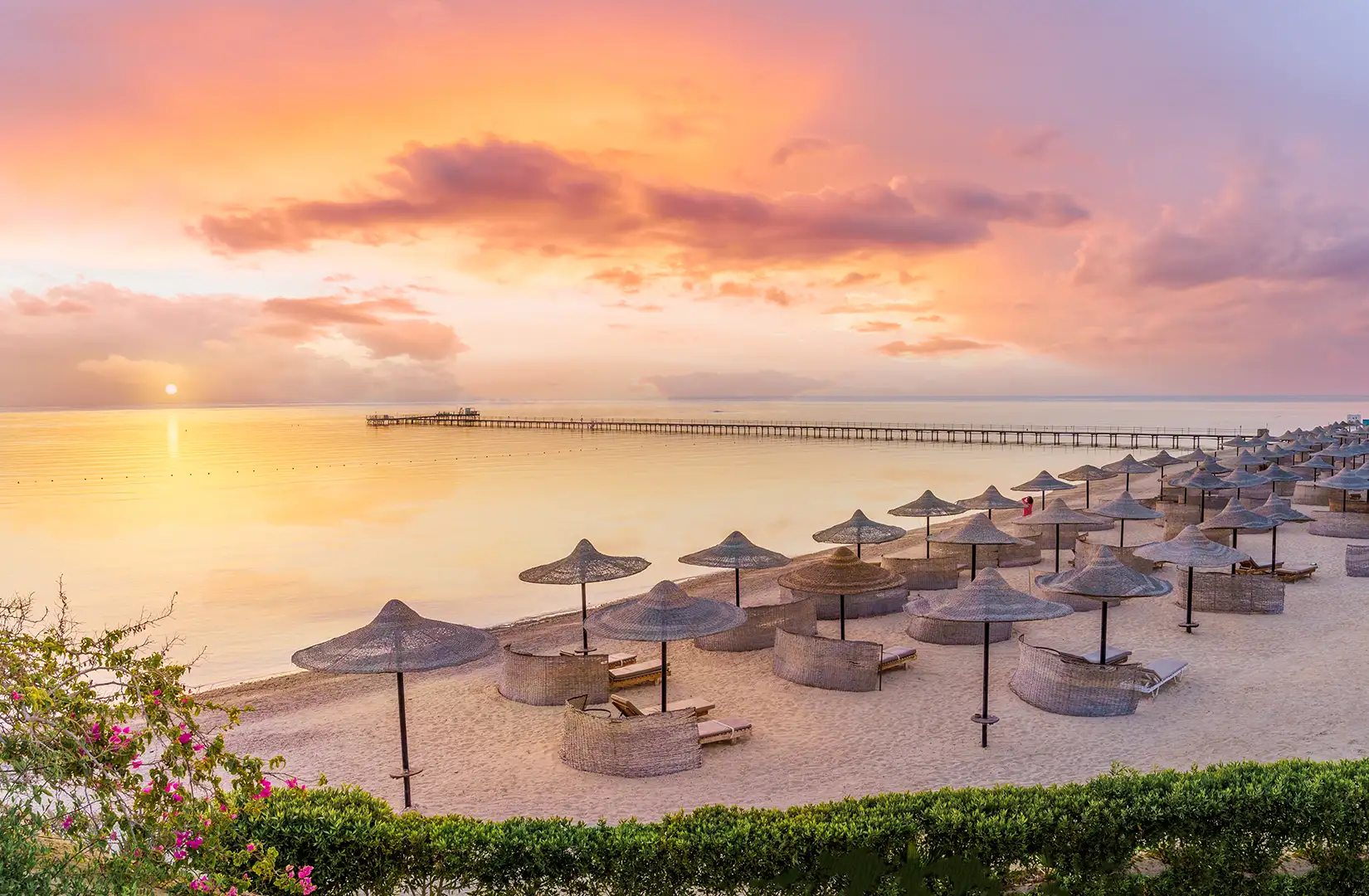 Sonnenuntergang am einem Strand mit Sonnenschirmen und Steg